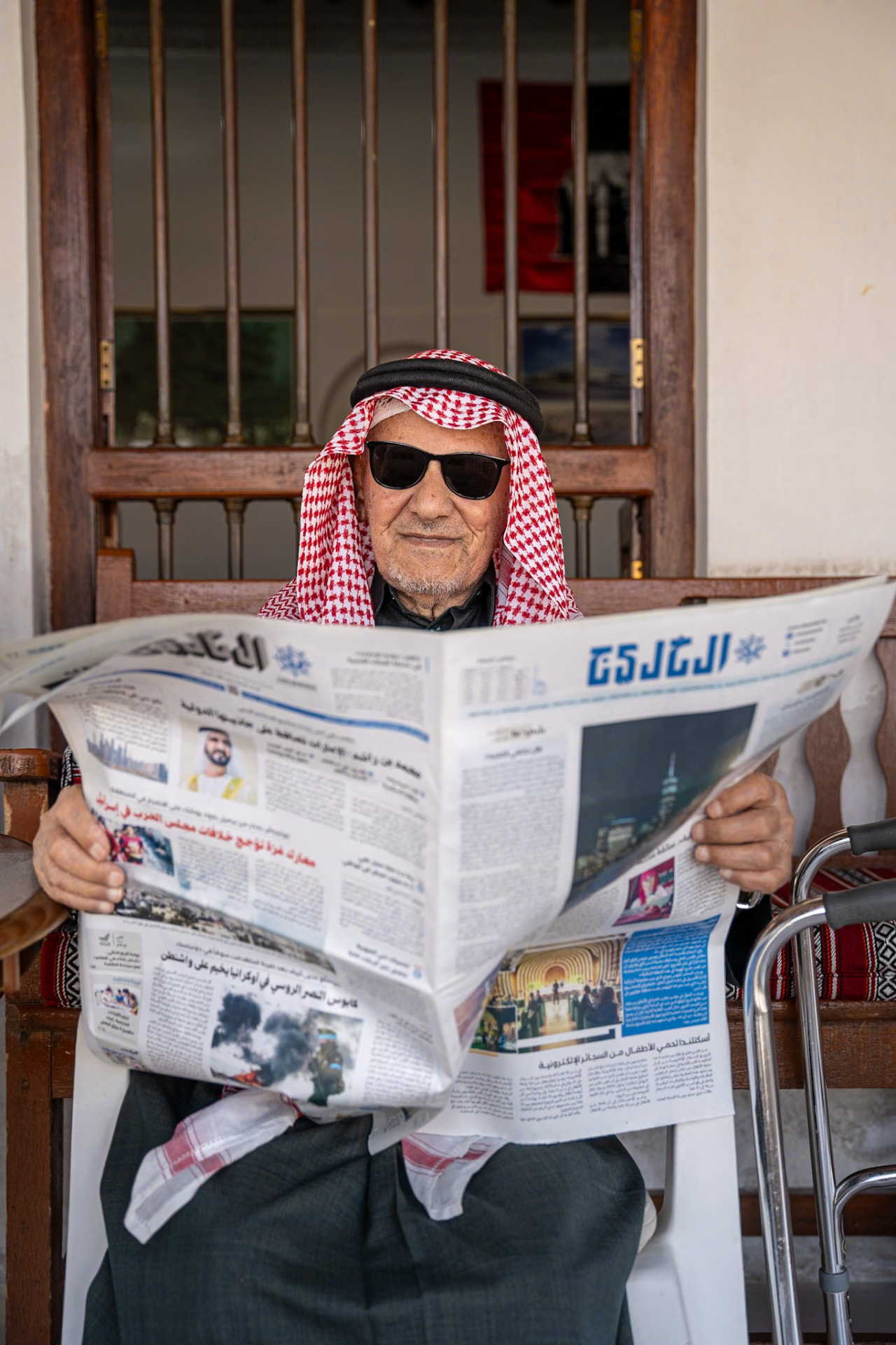 Elderly Emirati man in sunglasses reading an Arabic newspaper