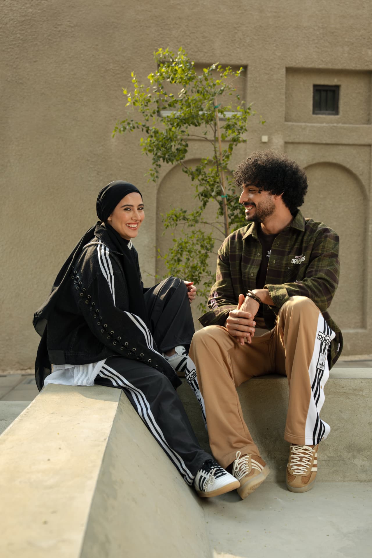 Couple in Adidas tracksuits sitting on a sandstone ledge