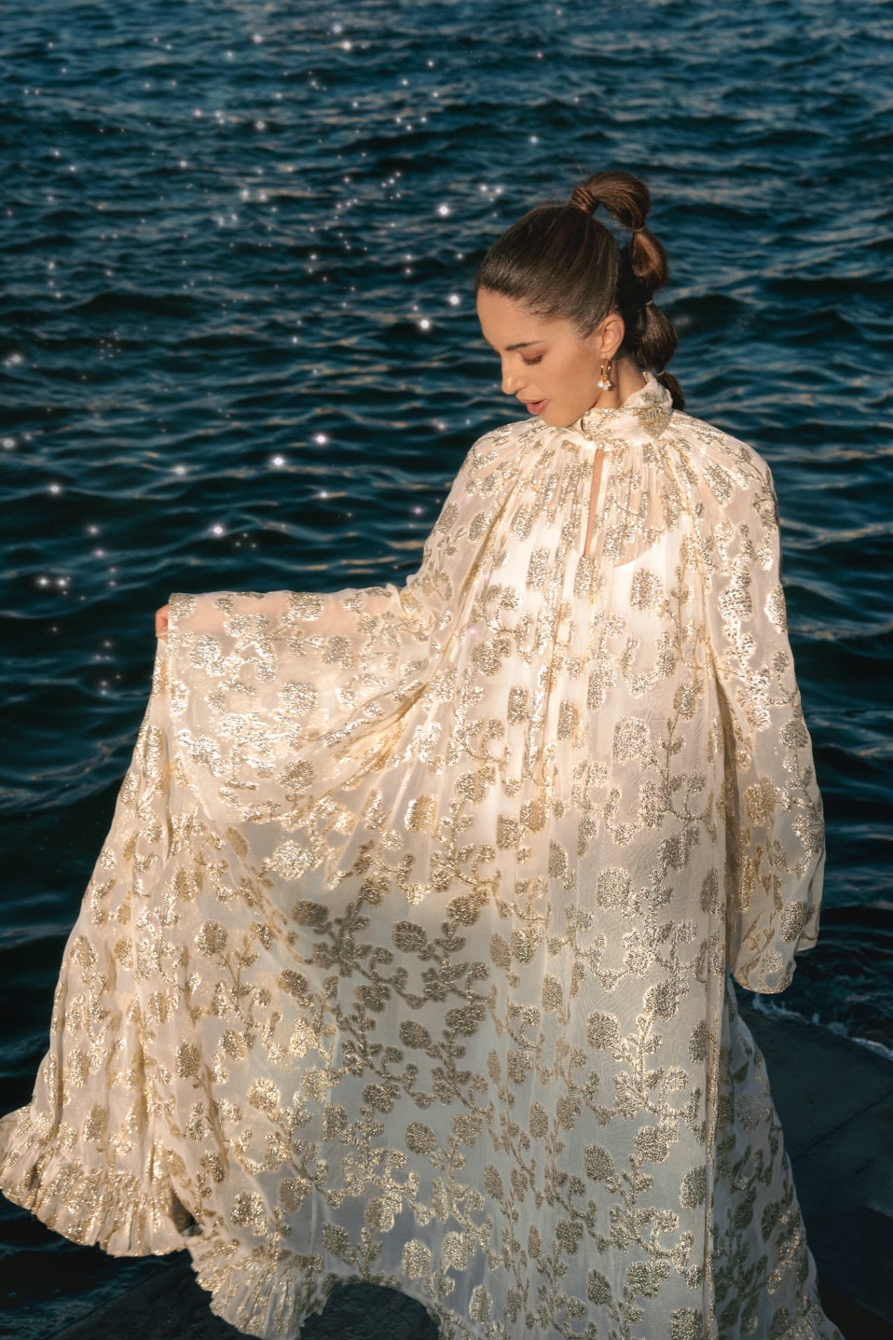 Woman in a gold brocade gown by the dark sea