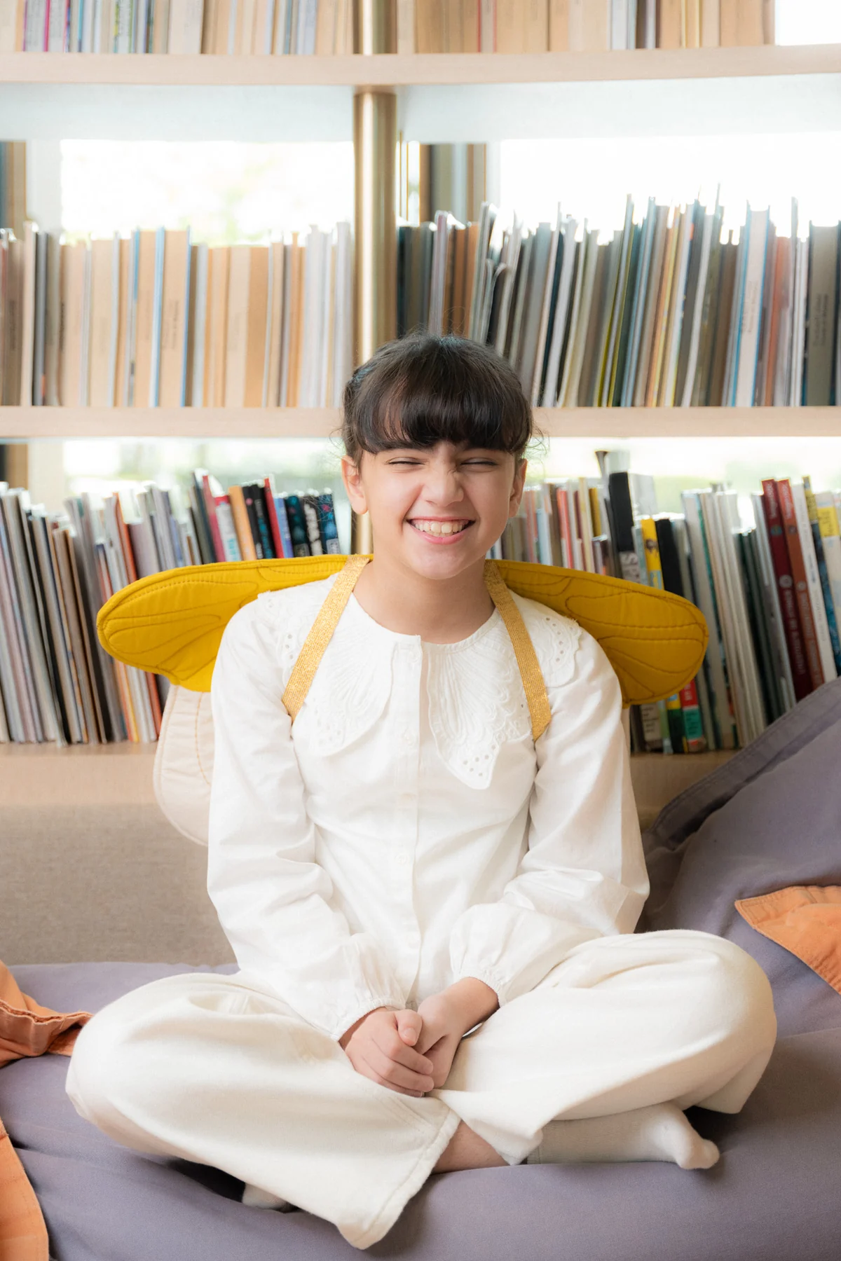 Smiling girl in white with yellow sleeves in a library