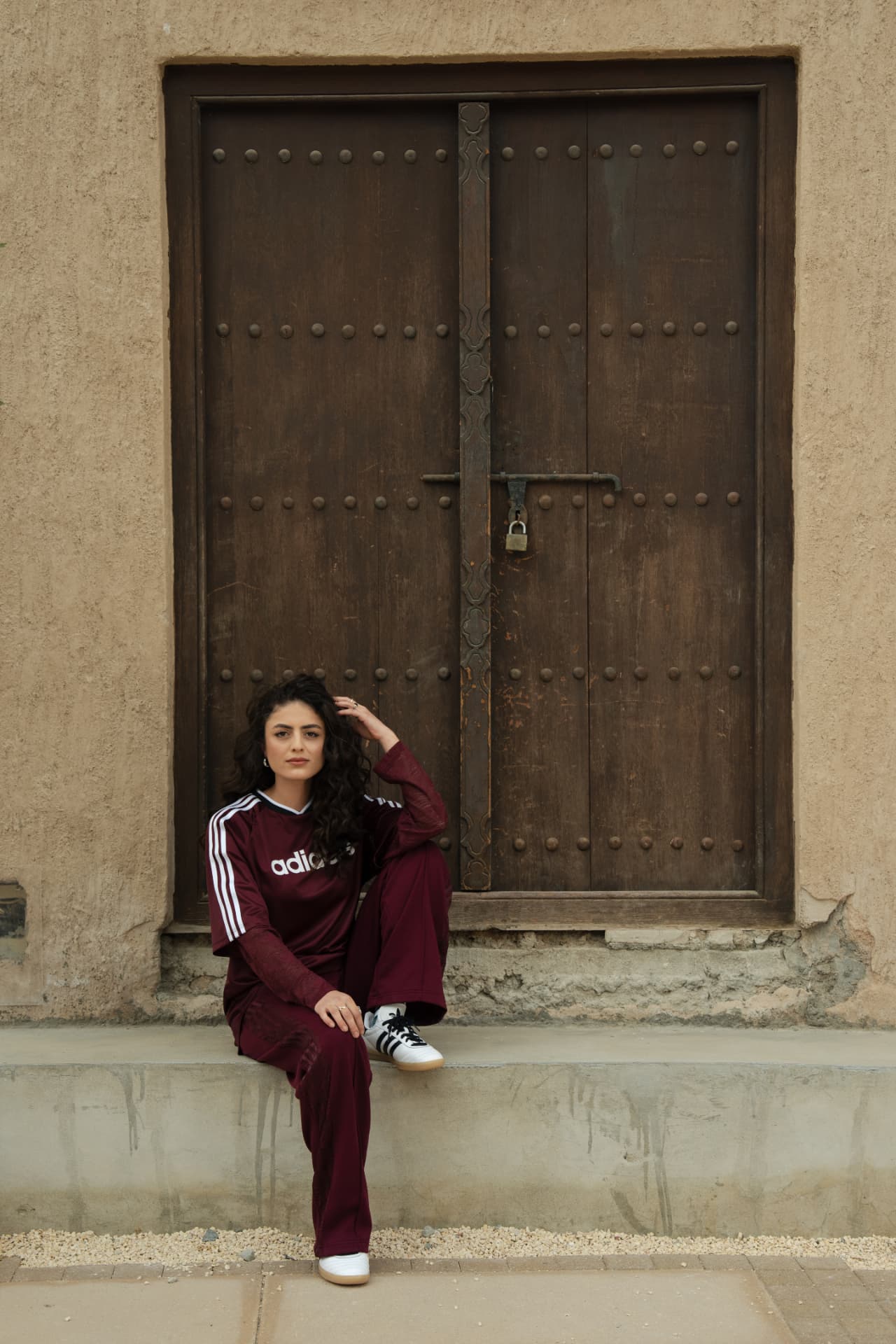 Woman in a maroon Adidas tracksuit before a wooden door