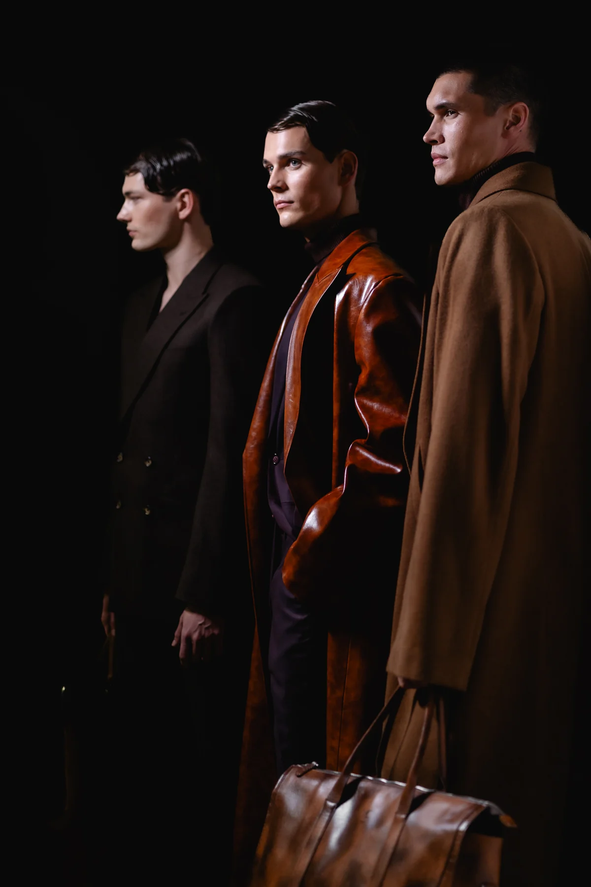 Three men in coats with a leather bag