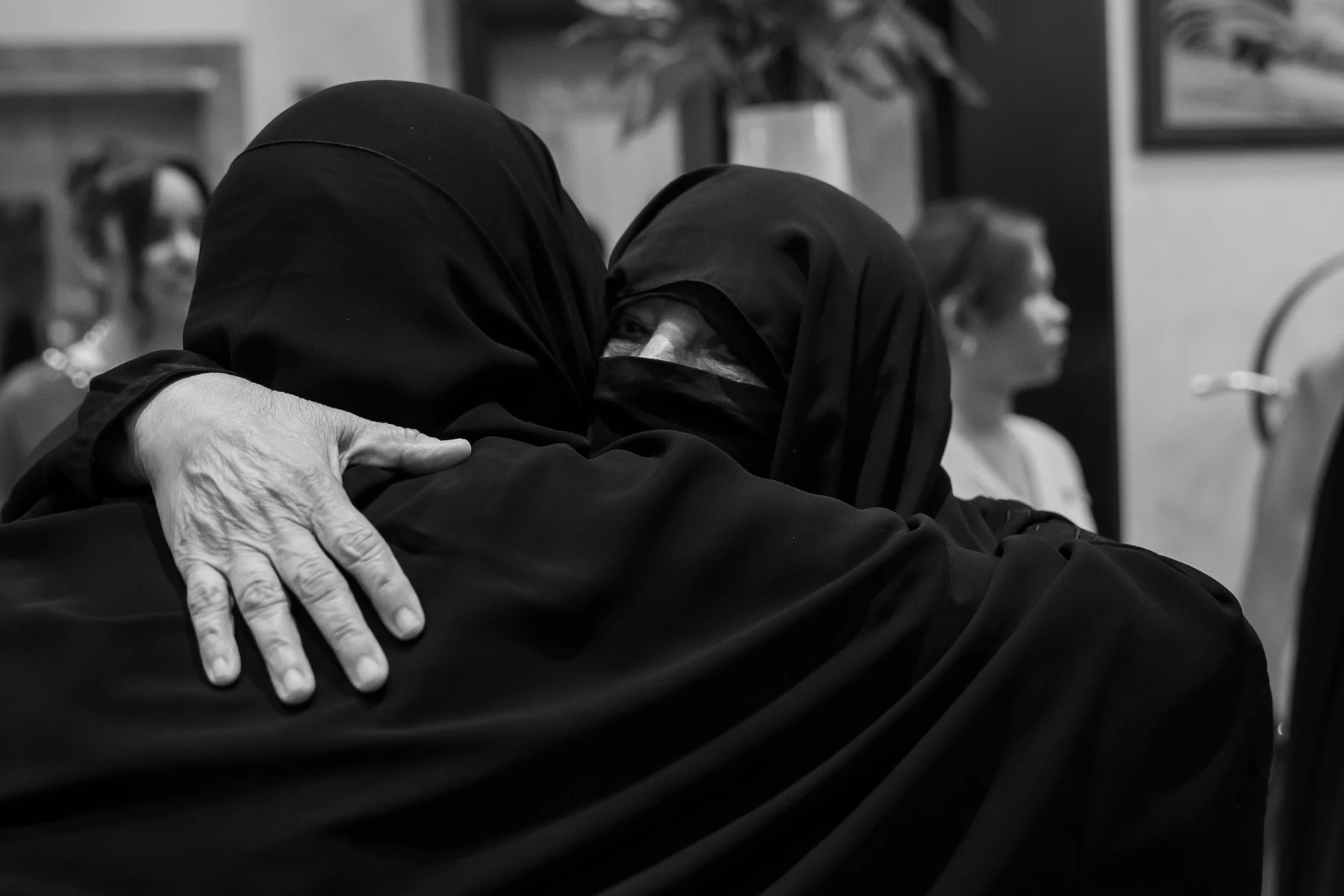 Two women in abayas embracing, black and white