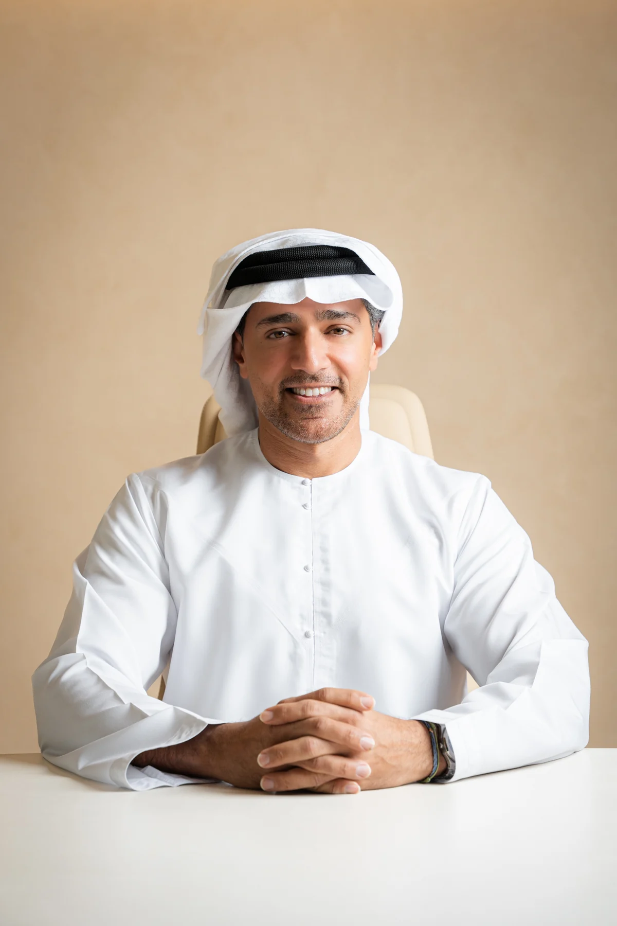 Emirati executive smiling at a white desk against a warm beige backdrop