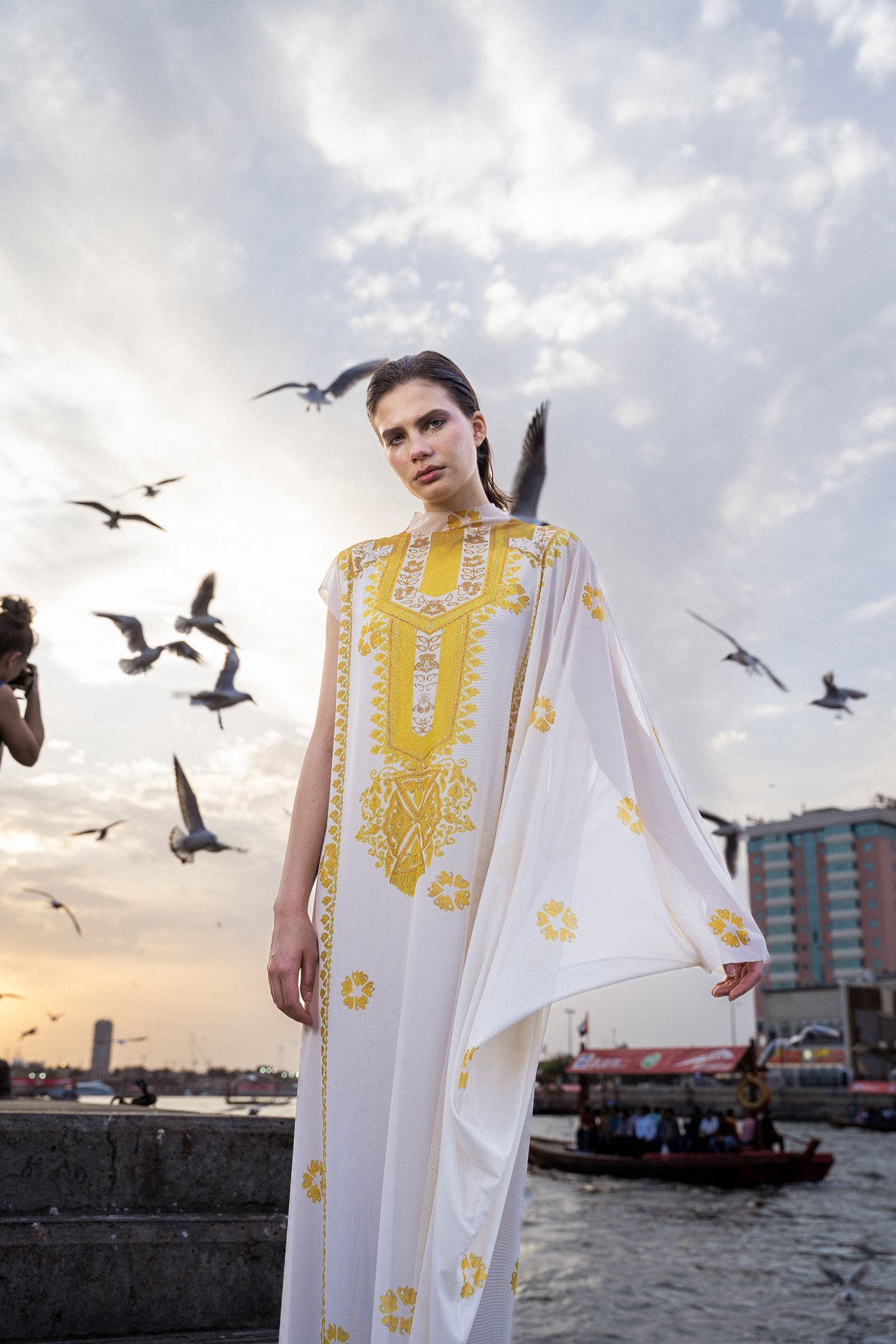 Model in white kaftan by the creek with gulls at sunset