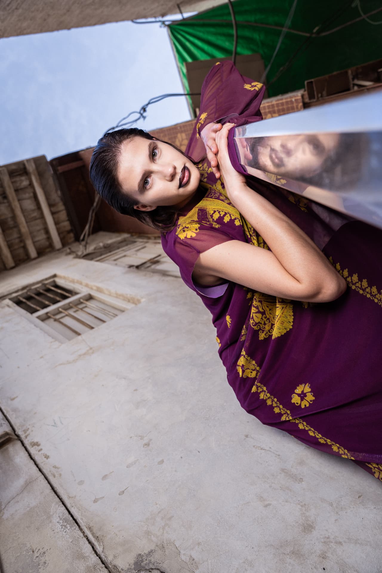 Model in purple kaftan photographed from below against old buildings