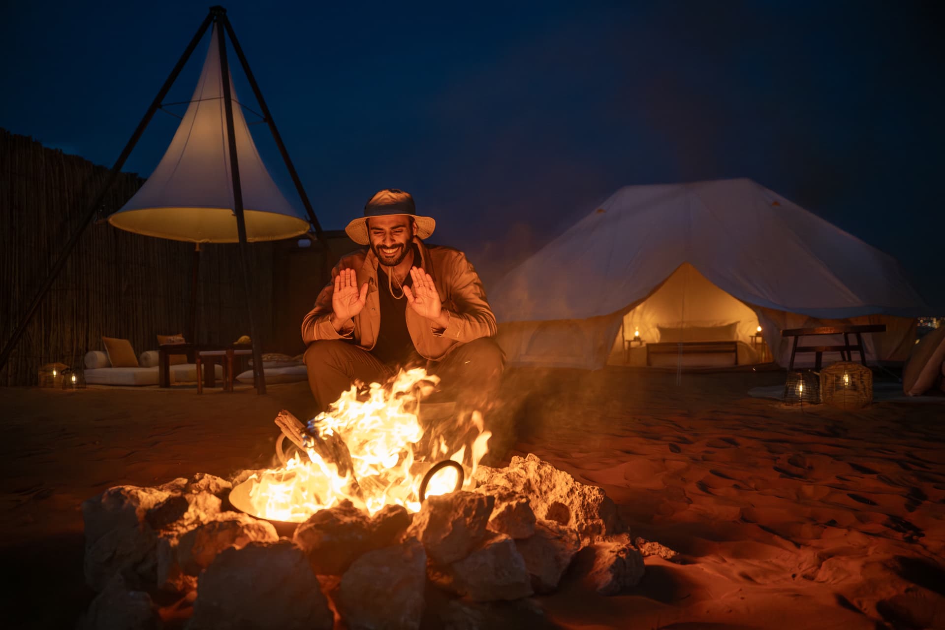 Man seated behind a roaring campfire at a desert camp
