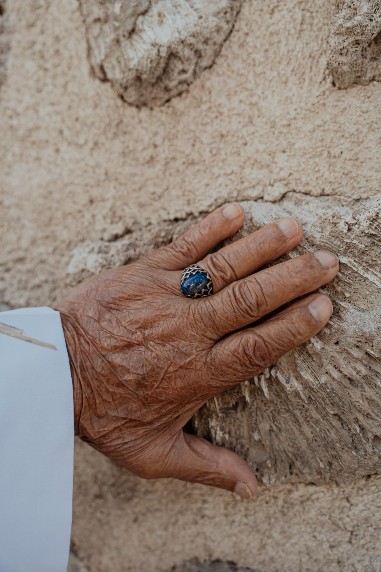 Weathered hand with a blue ring resting on a stone wall