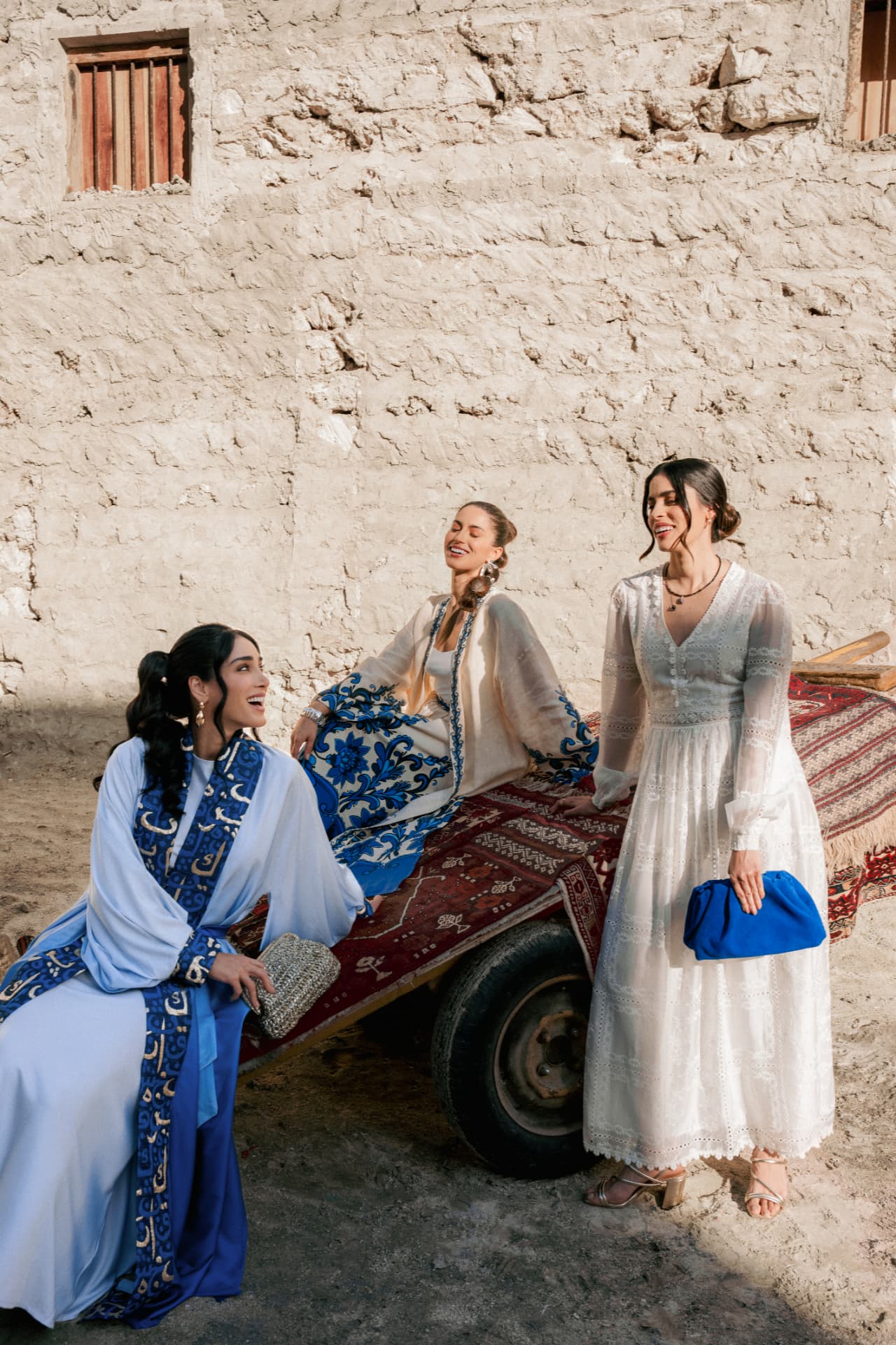 Three women in white and blue by a cart against a sandstone wall