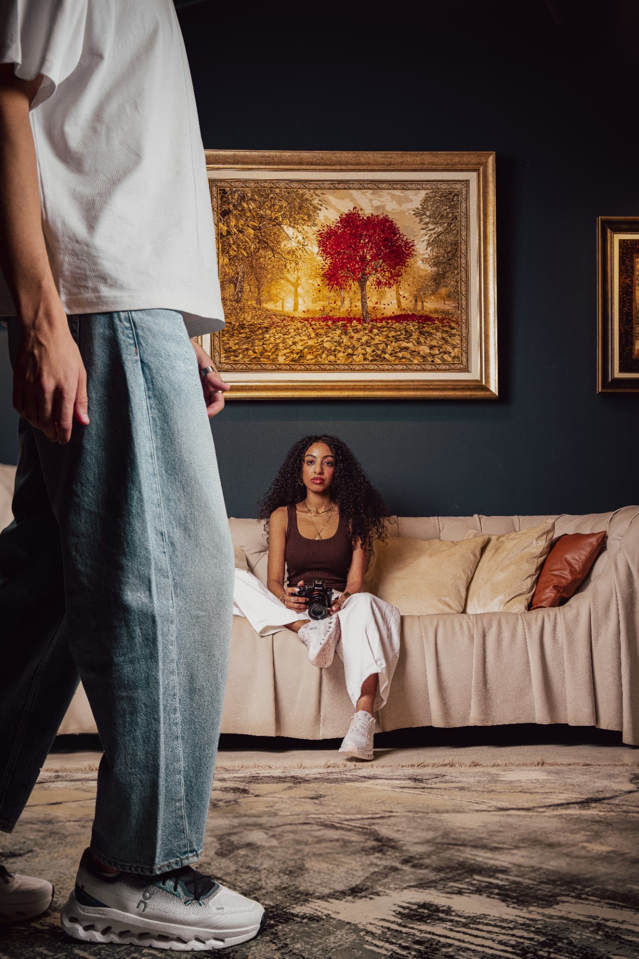 Model's legs and sneakers before a woman on a sofa