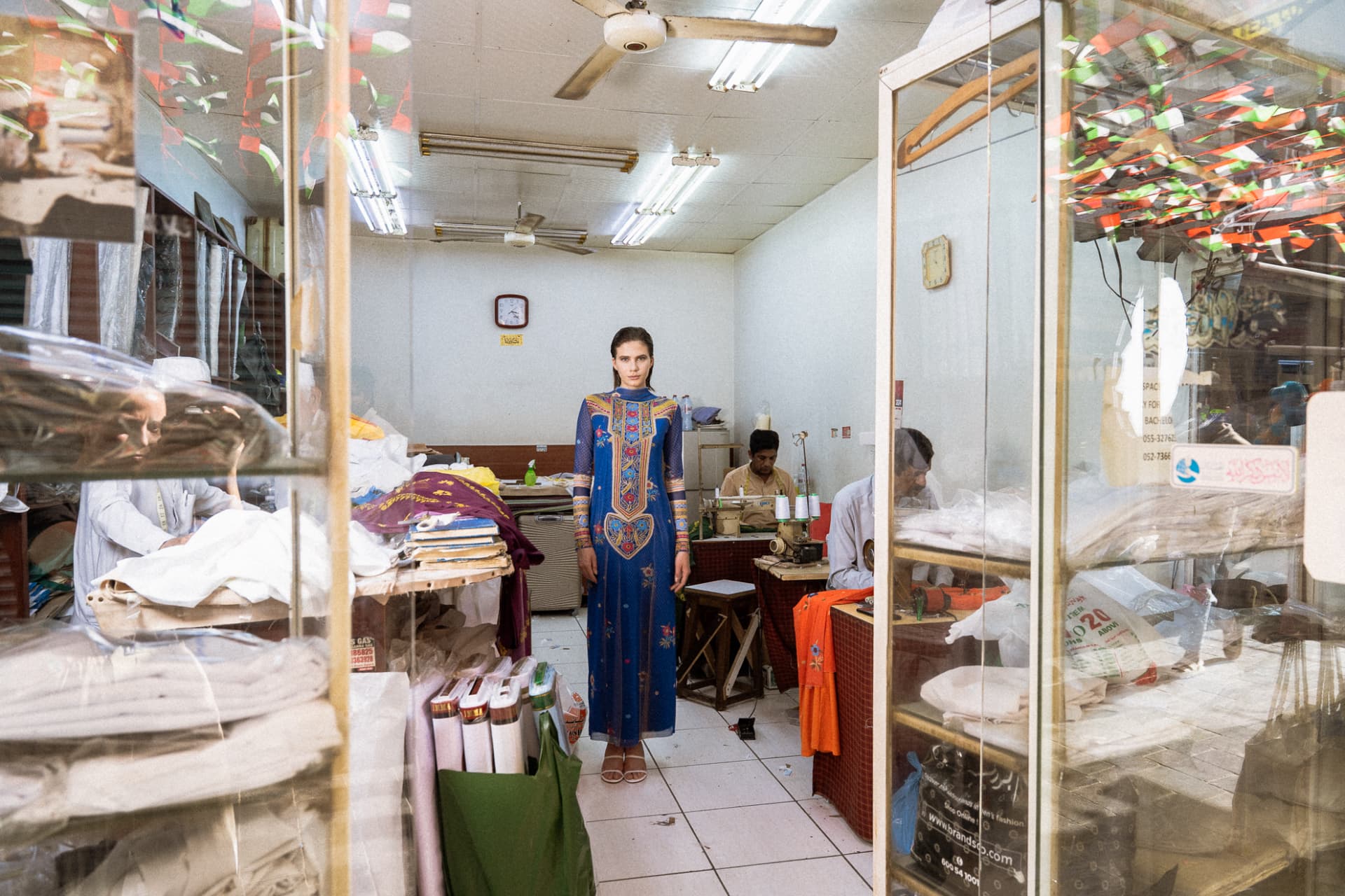 Model in blue embroidered dress inside a tailor's shop