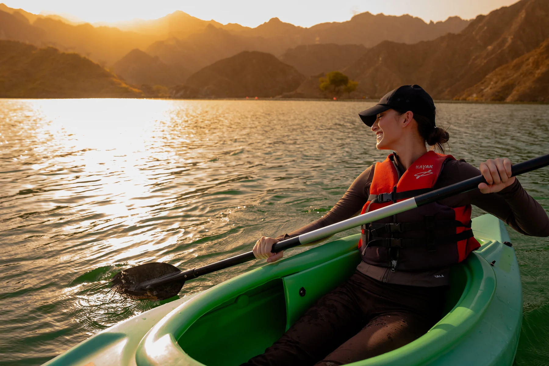 Woman paddling a green kayak at sunset among mountains